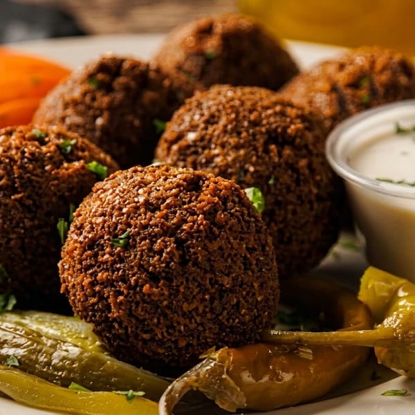 Plate of crispy falafel balls with pickled vegetables and a side of white dipping sauce.