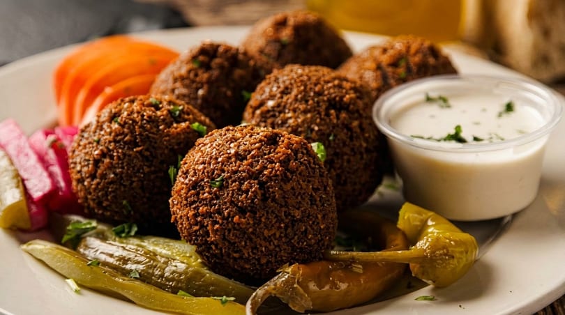 Plate of crispy falafel balls with pickled vegetables and a side of white dipping sauce.