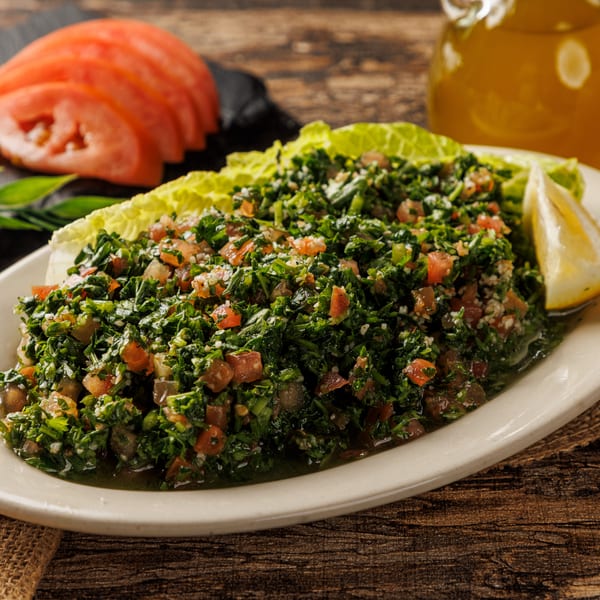 Tabbouleh salad with lemon, lettuce, and sliced tomatoes on a rustic wooden table with olive oil.