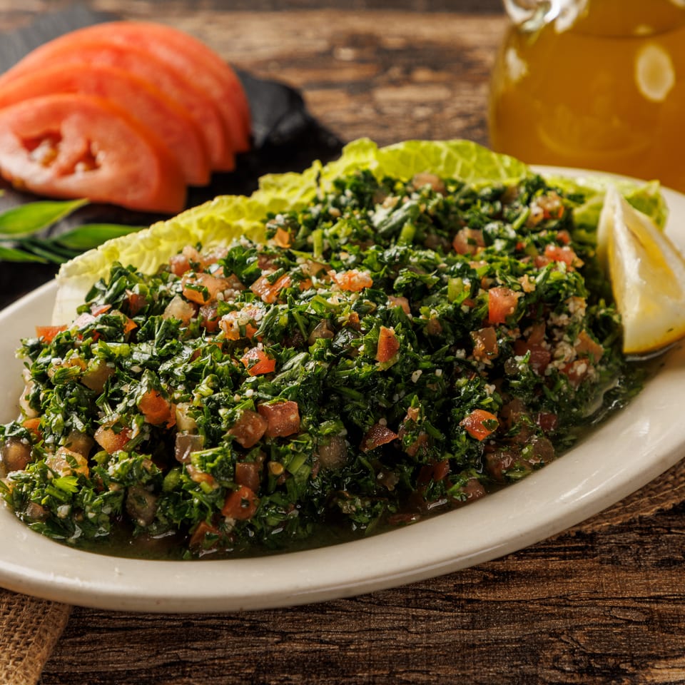 Tabbouleh salad with lemon, lettuce, and sliced tomatoes on a rustic wooden table with olive oil.