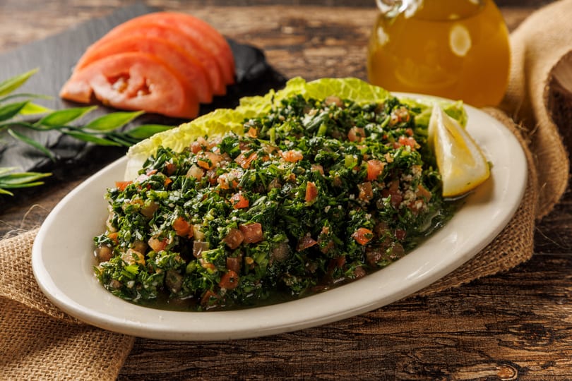 Tabbouleh salad with lemon, lettuce, and sliced tomatoes on a rustic wooden table with olive oil.