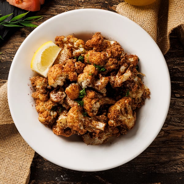 Seasoned roasted cauliflower with a lemon wedge on a white plate, set on a rustic wooden table.