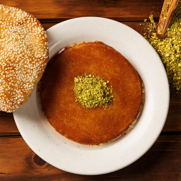 Kunafa dessert with pistachios, sesame flatbread, and ground pistachios on a wooden table.