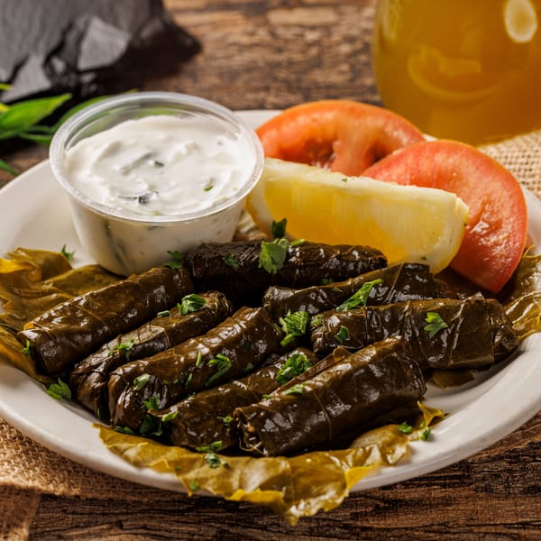Plate of dolmades with tzatziki, lemon, and tomato slices on a rustic wooden table.