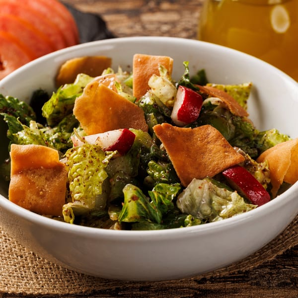 Fresh Fattoush salad in a white bowl with lettuce, radishes, and crispy pita bread.