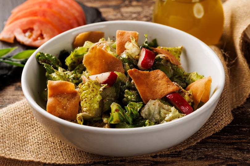 Fresh Fattoush salad in a white bowl with lettuce, radishes, and crispy pita bread.